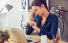 Frustrated young woman keeping eyes closed and massaging nose while sitting at her working place in office