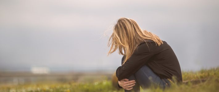 Side view of a despaired woman sitting curled up in nature.