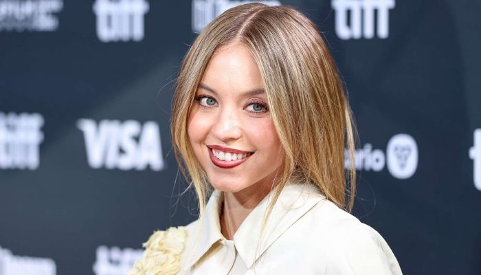 Skådespelerskan Sydney Sweeney ler lugnt framför en mörk bakgrund.